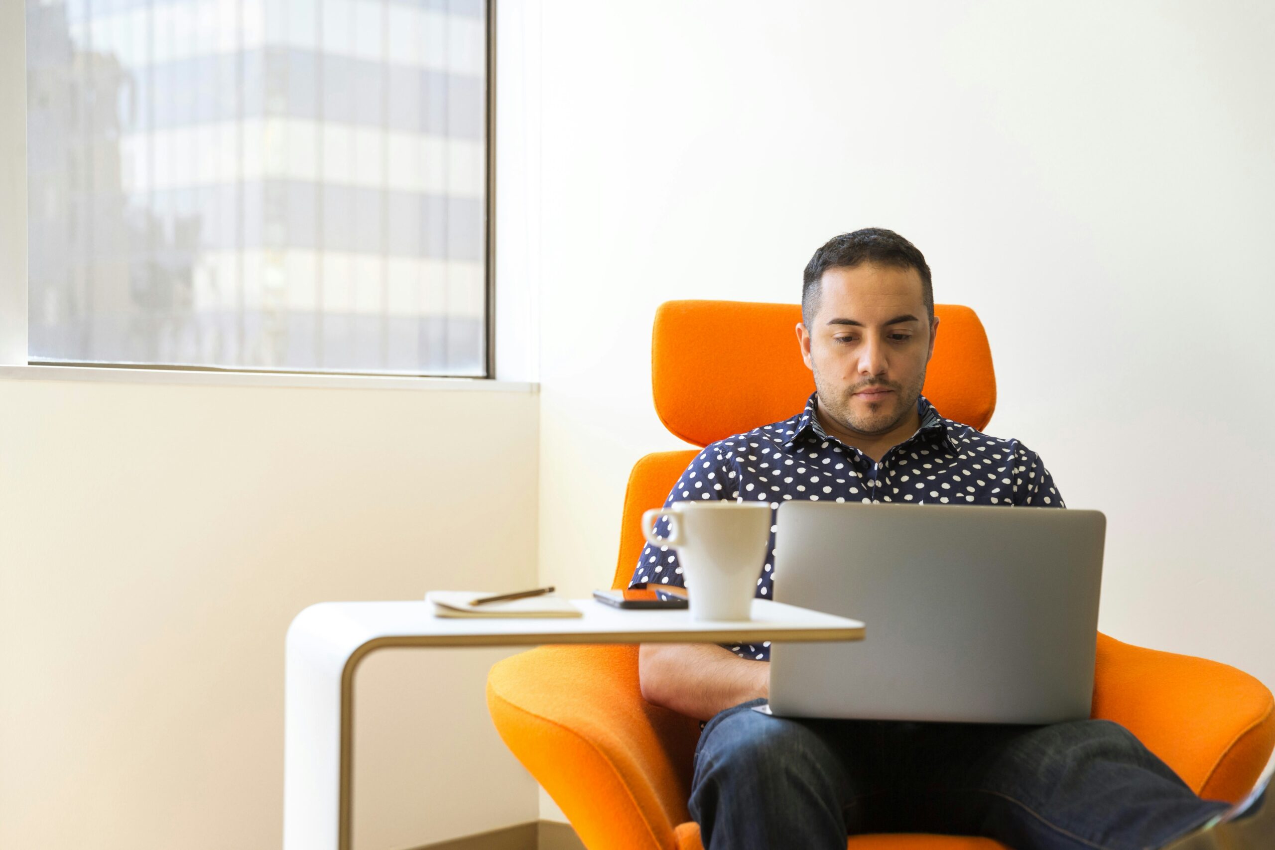 Man sitting in an orange chair using a laptop