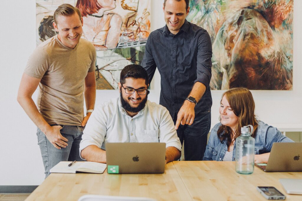 A group of colleagues happily review data on a laptop, symbolizing collaboration in analyzing the success of social media customer acquisition strategies.