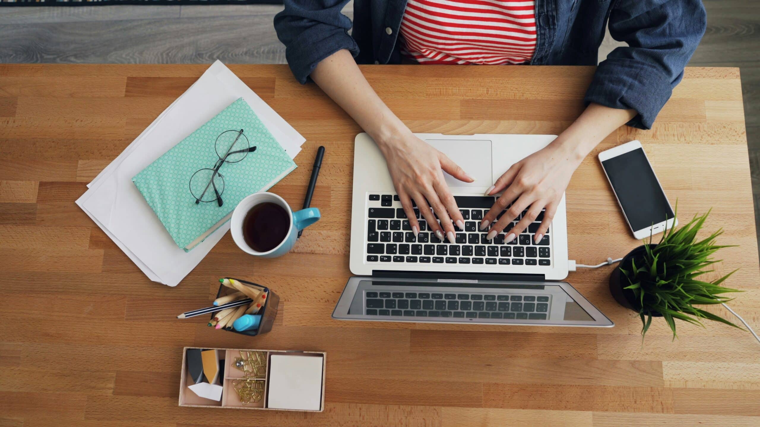 Top-down view of a workspace with woman typing on laptop