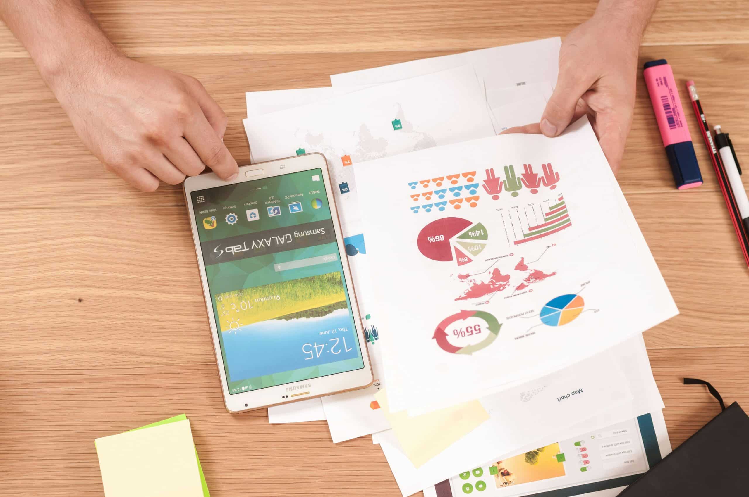 A person reviews colorful infographic reports and uses a tablet, representing the process of defining specific conversion goals for each landing page based on data insights.