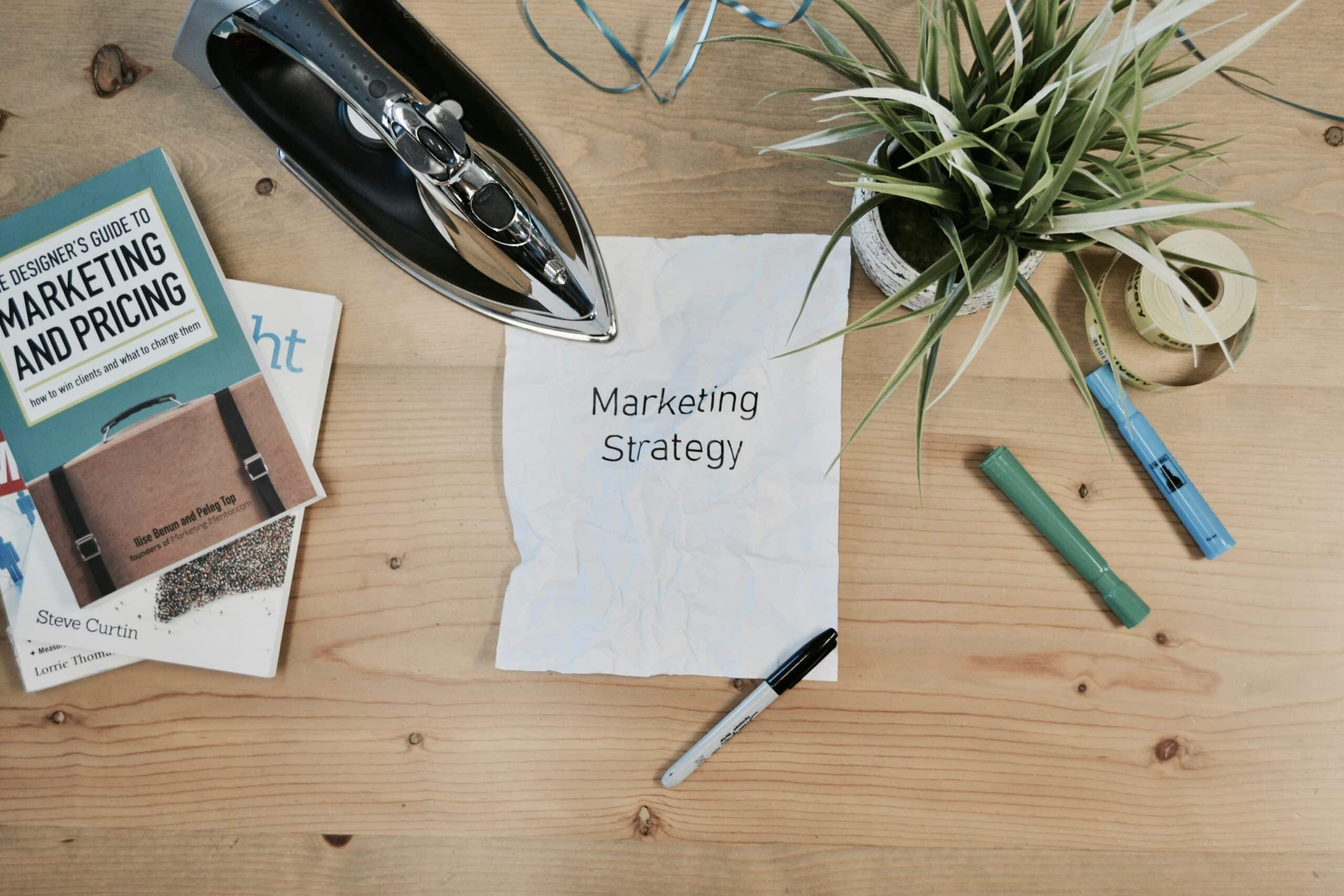 A crumpled paper labeled “Marketing Strategy” surrounded by planning tools and books, symbolizing the refinement process of aligning sales and marketing with an ideal customer profile. - Nurture Machines A crumpled paper labeled “Marketing Strategy” surrounded by planning tools and books, symbolizing the refinement process of aligning sales and marketing with an ideal customer profile.