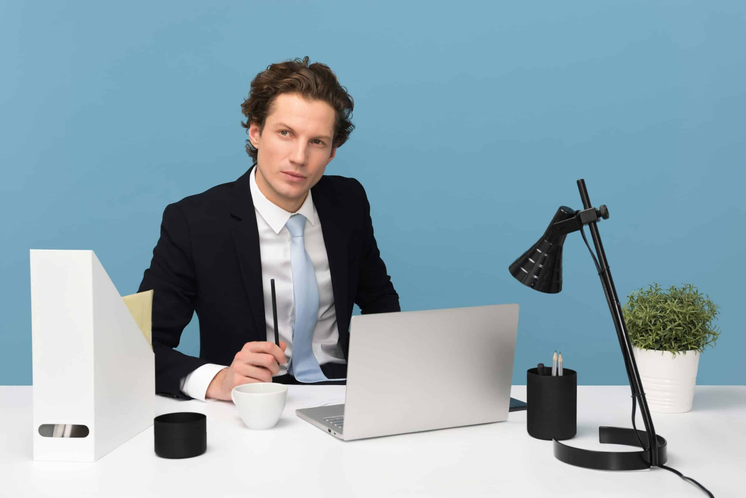 A professional focused on his laptop in a modern office. - Nurture Machines A business professional at a desk with a laptop and notes, reflecting on strategic questions to define an ideal customer profile for targeted marketing.