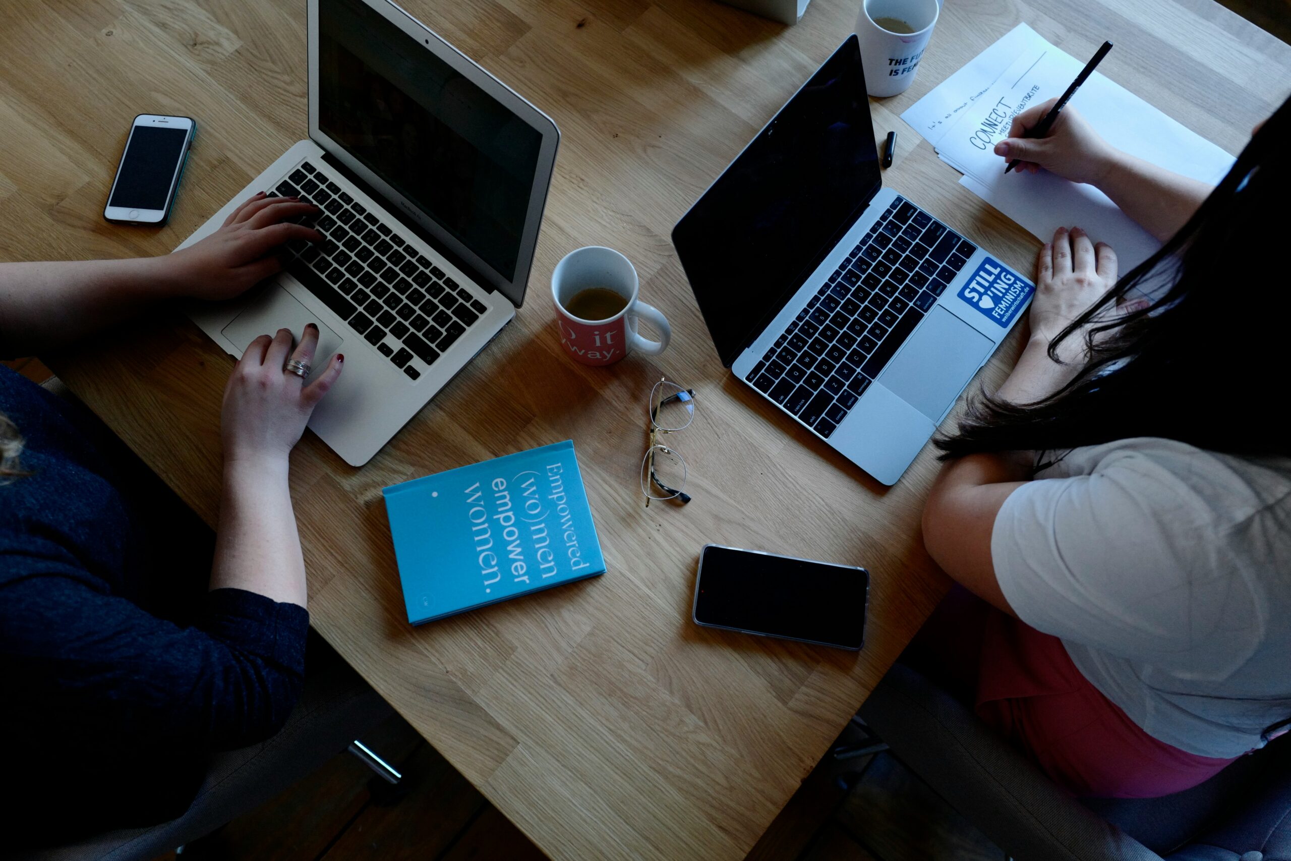 Two people working on laptops and reviewing notes at a desk—highlighting the importance of regularly reassessing and refining customer acquisition strategies.