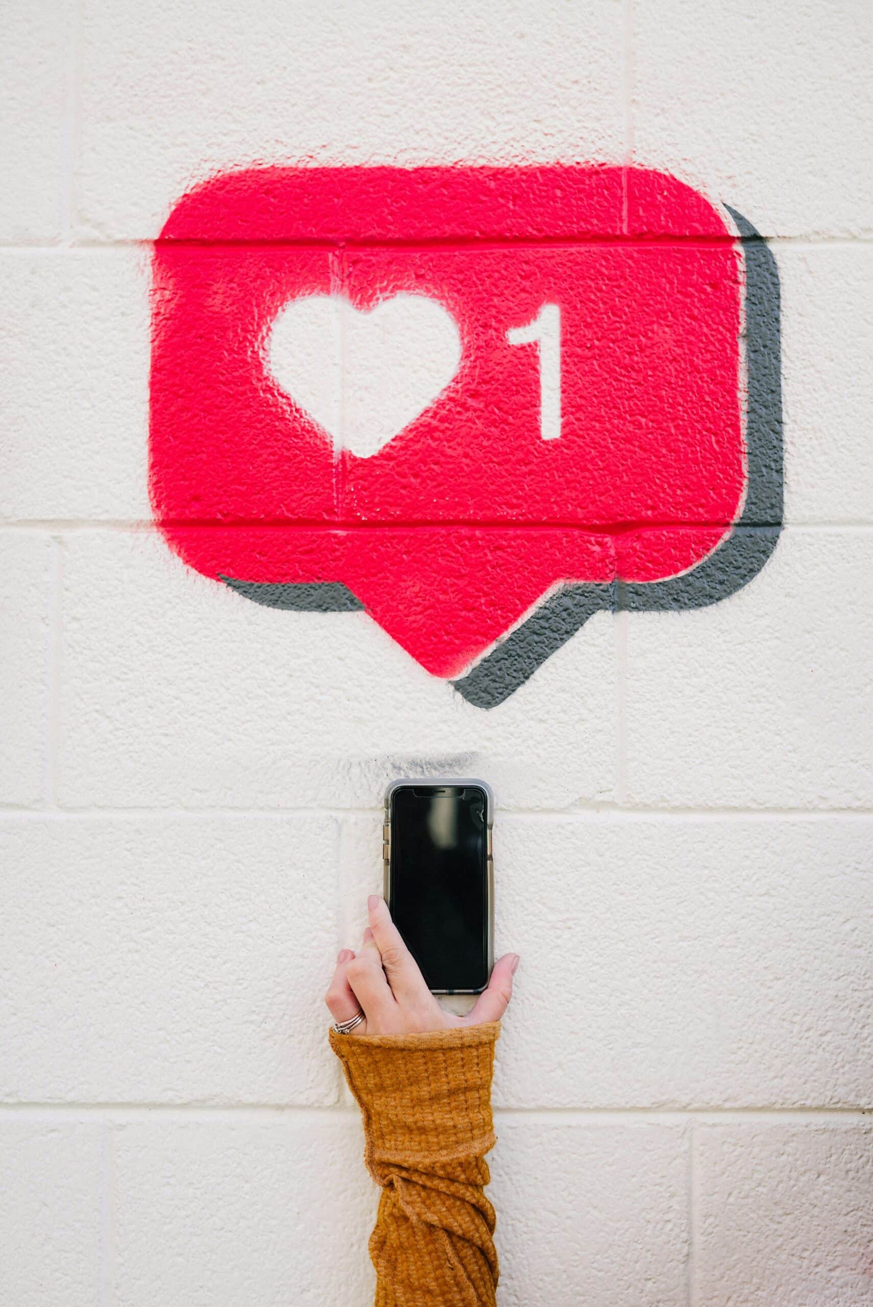 A hand holding a smartphone beneath a painted social media like icon, symbolizing the role of paid ads and campaigns in accelerating customer growth.