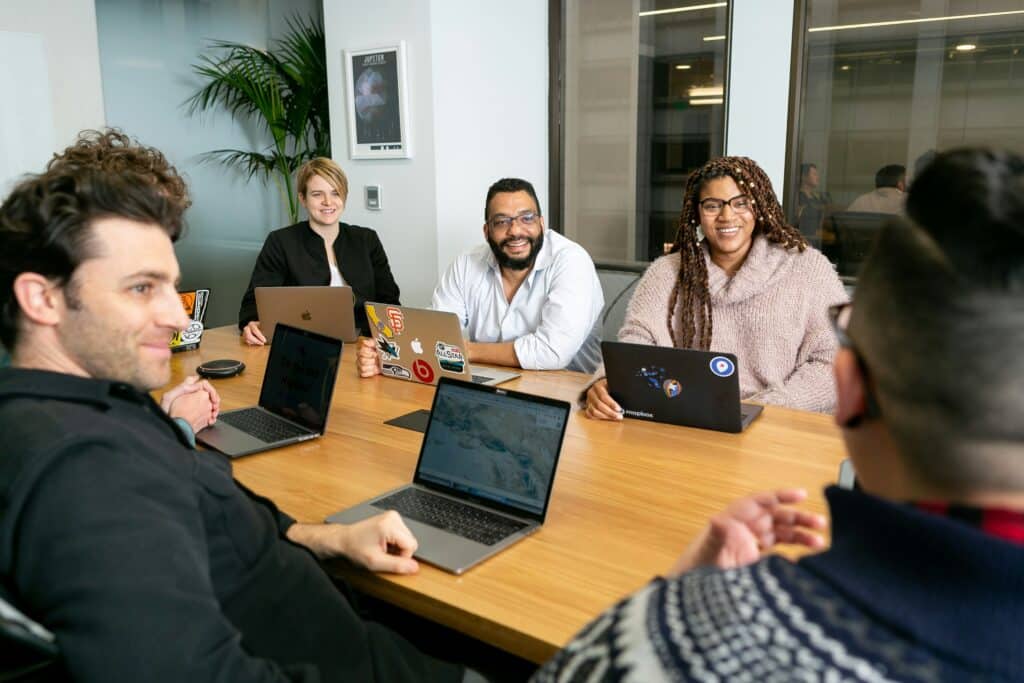 A diverse team collaborates around a conference table with laptops, emphasizing the value of group analysis in spotting and understanding evolving market trends.