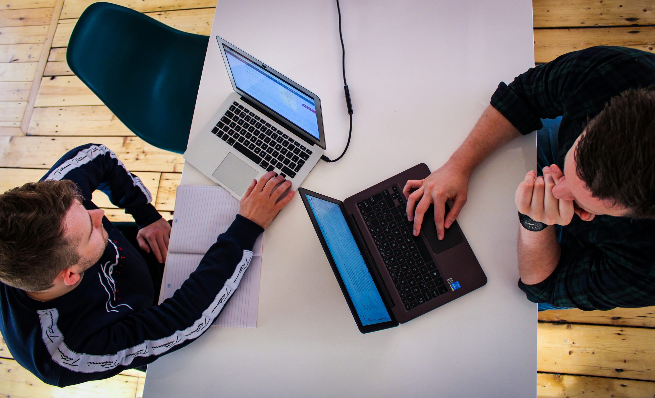 Two professionals analyze data on their laptops to compare the performance of various acquisition channels against industry competitors.