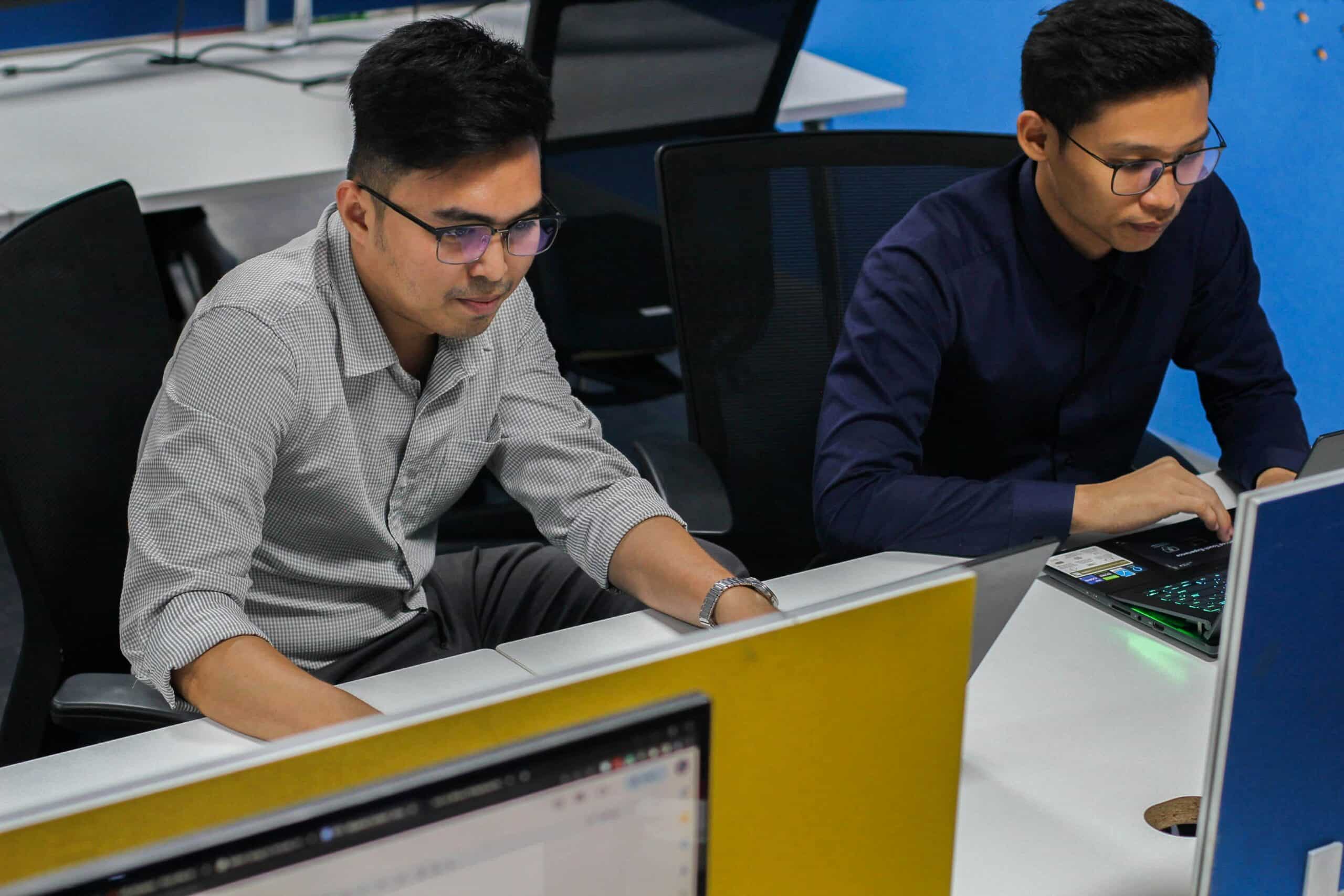 Two professionals focused on their laptops in a modern office, representing strategic collaboration to overcome lead generation and conversion challenges. - Nurture Machines Two professionals analyze data on their laptops in an office setting, representing the process of identifying an ideal customer profile through data-driven insights.