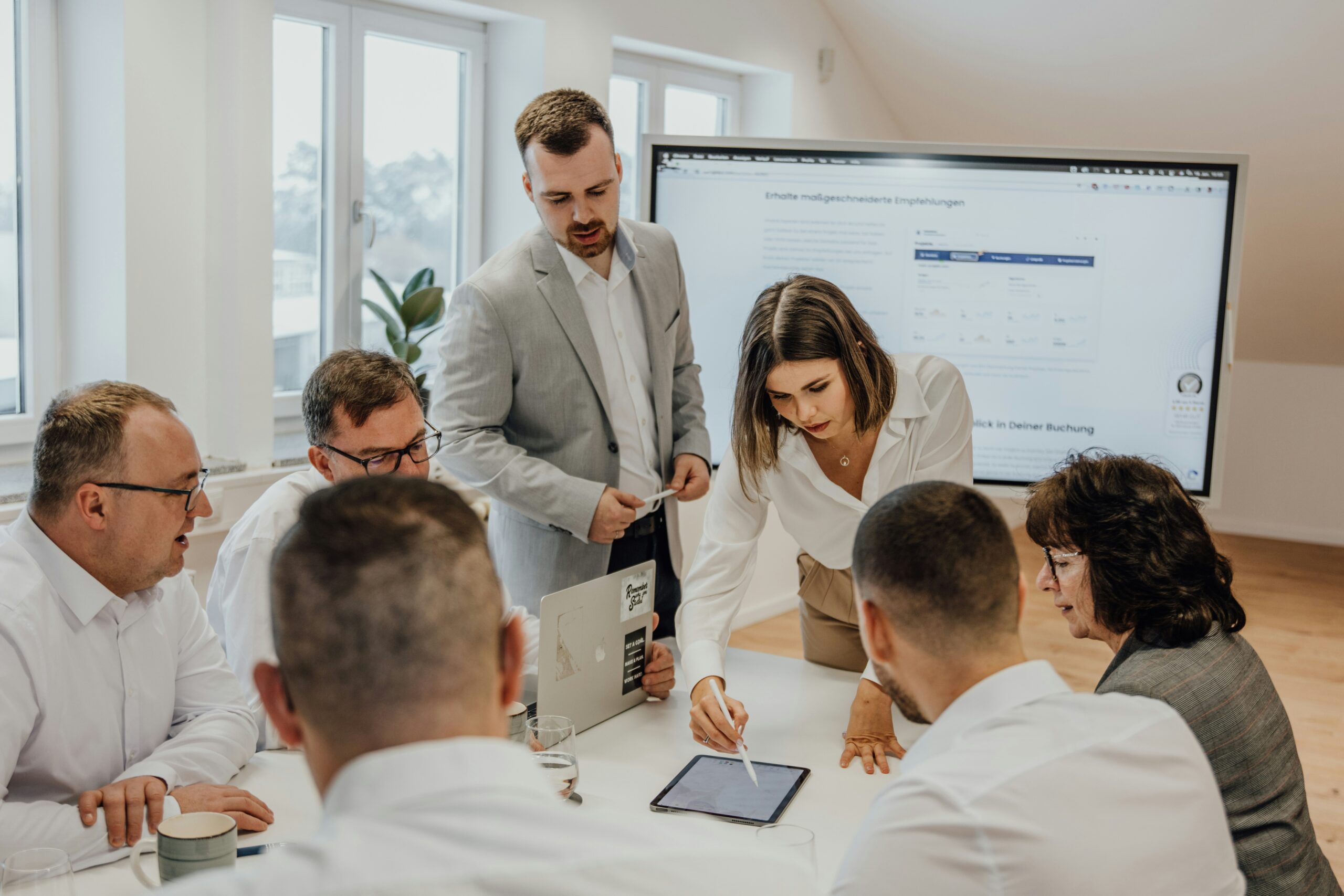A group of professionals gathered around a tablet in a meeting room, analyzing digital strategies to compare and evaluate top-performing customer acquisition channels.