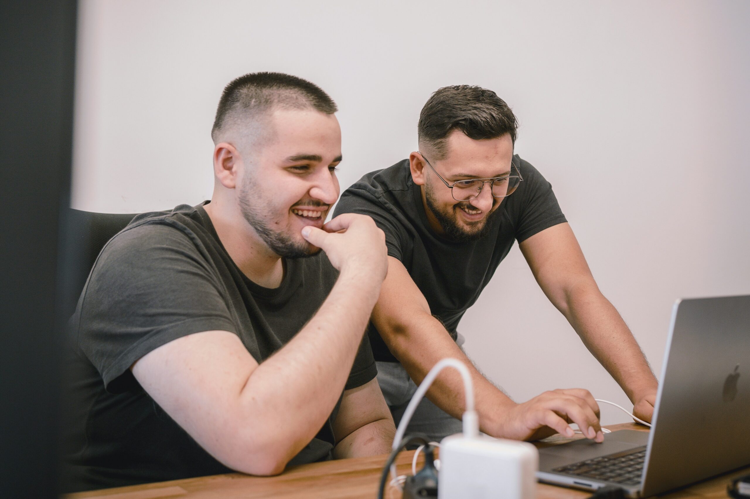 Two team members smiling while analyzing data on a laptop, representing the process of mapping customer journeys to refine and enhance marketing messages.